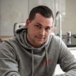 Man in gray hoodie in kitchen setting.