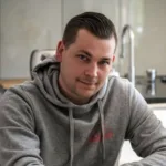 Man in gray hoodie in kitchen setting.